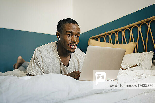 Mid adult man using laptop over bed in bedroom