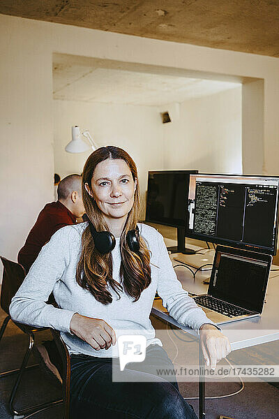 Porträt einer Programmiererin mit Laptop und Computer am Schreibtisch im Büro