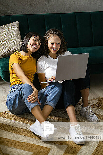 Smiling lesbian couple using laptop while sitting on carpet at home