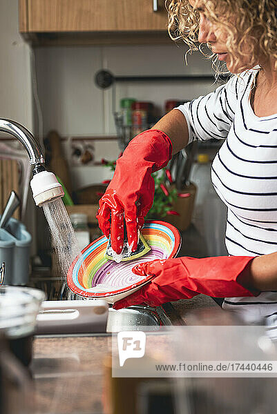 Woman cleaning plate at sink in kitchen