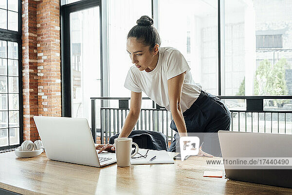 Female business professional using laptop while standing at desk in office