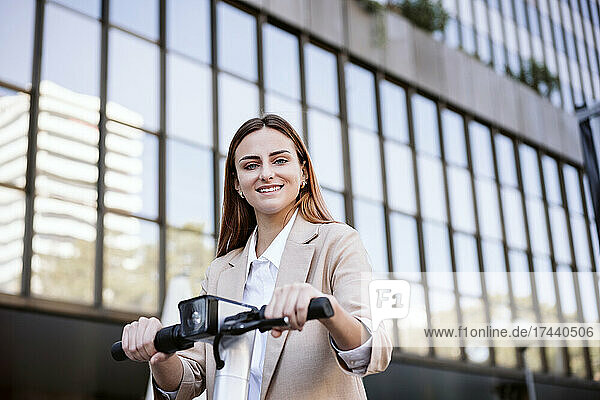 Smiling businesswoman with electric push scooter in city
