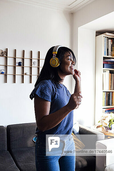 Smiling mid adult woman listening music through wireless headphones while dancing in living room