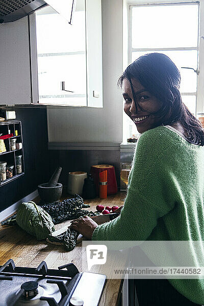 Smiling woman cutting kale in kitchen