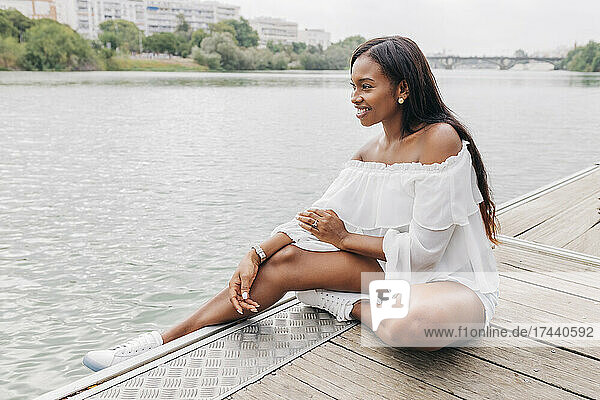 Smiling mid adult woman sitting on pier by lake