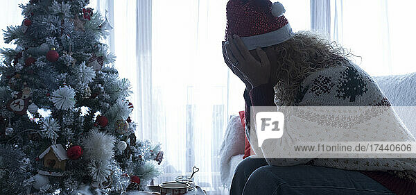 Frau mit Kopf in den Händen sitzt zu Hause auf dem Sofa