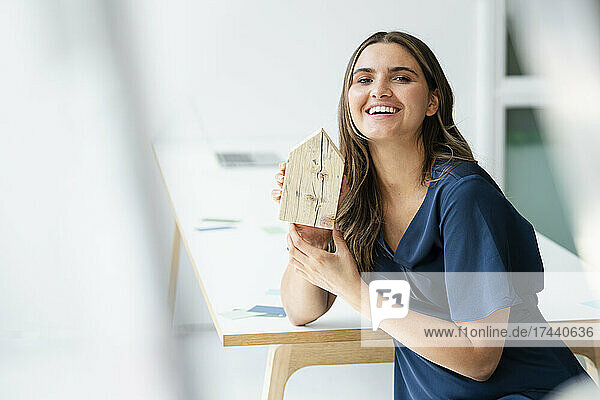 Lächelnde Architektin hält Hausmodell am Schreibtisch