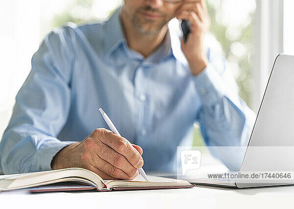 Mature businessman writing in diary at desk in office