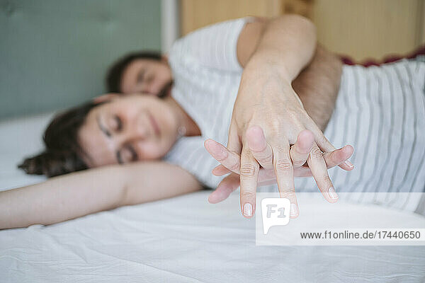 Mid adult couple with hands clasped lying on bed at home