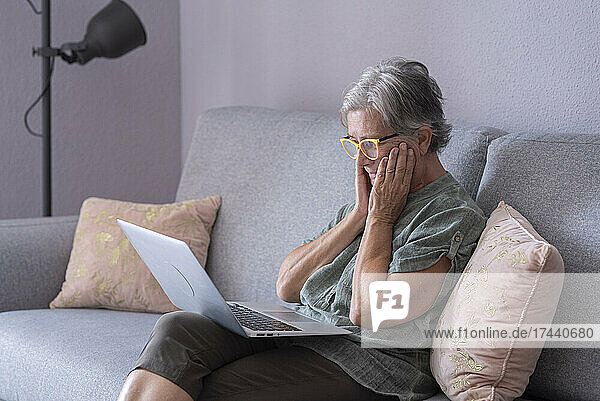 Worried woman with laptop sitting on sofa in living room