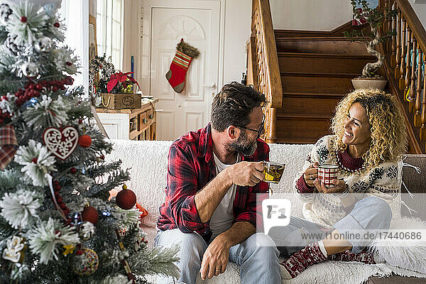 Smiling woman having coffee with man while sitting on sofa at home during Christmas