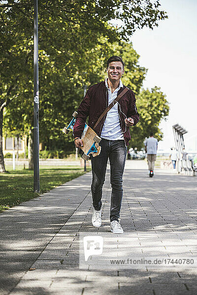 Man with skateboard walking on footpath