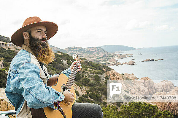 Man wearing hat playing guitar while looking at view
