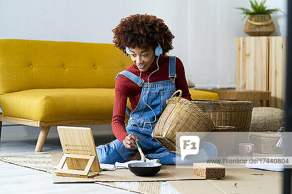 Redhead woman learning to paint wicker basket through digital tablet at home