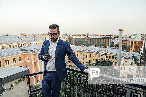 Male professional with smart phone leaning on railing in balcony