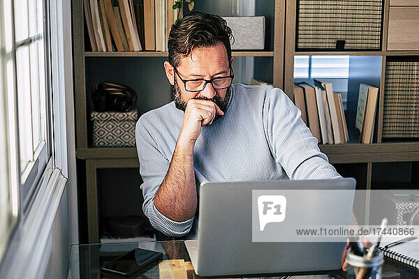 Male professional with hand on chin working on laptop at home