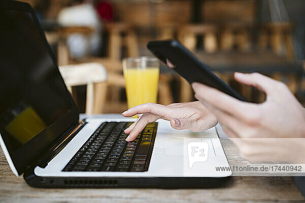 Businesswoman with mobile phone using laptop at coffee shop