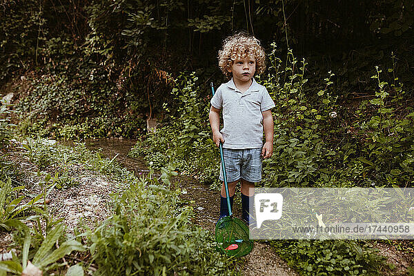 Boy with fishing net looking away while standing amidst plants