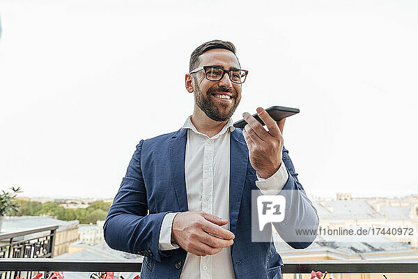 Smiling businessman sending voicemail through smart phone