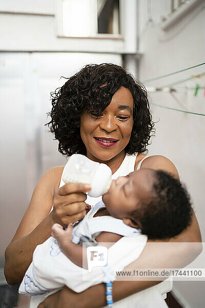 Smiling mature woman feeding milk to baby boy at home
