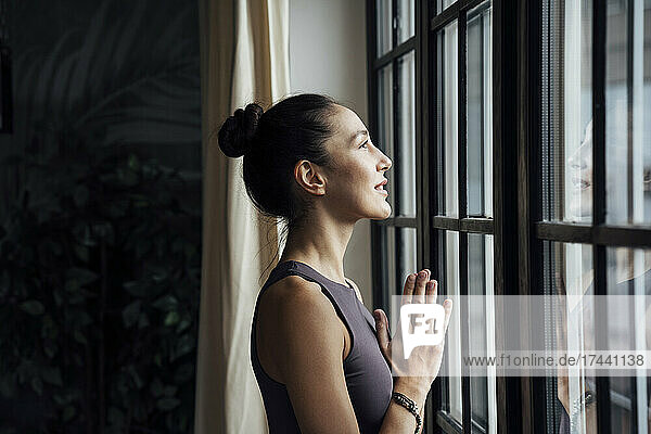 Woman with hands clasped looking through window