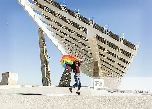 Woman holding rainbow flag near solar energy panel