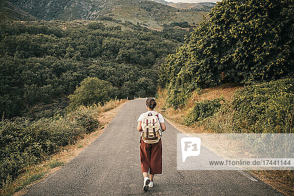 Female tourist wearing backpack looking at mountain while walking on road