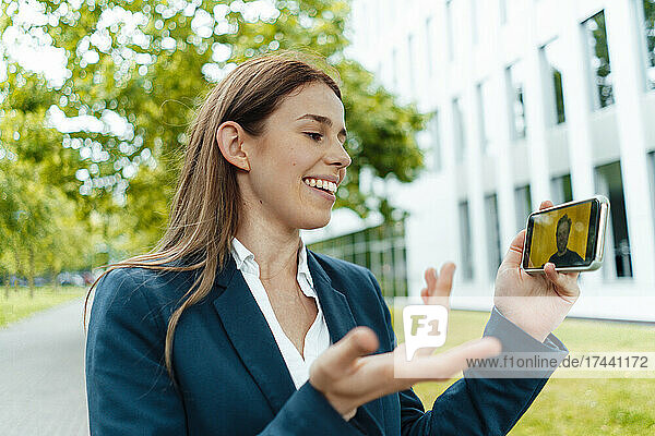 Smiling businesswoman gesturing during video call through mobile phone at public park