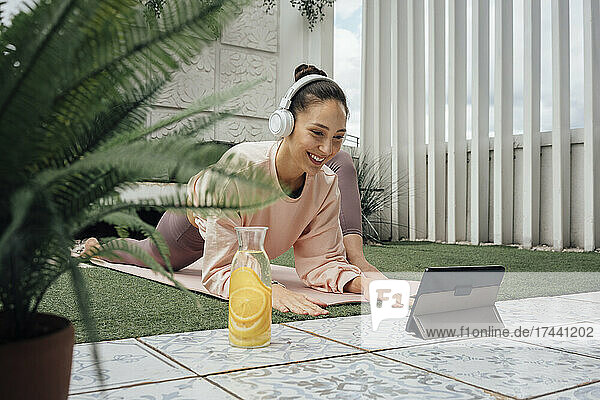 Smiling woman wearing headphones practicing yoga on terrace