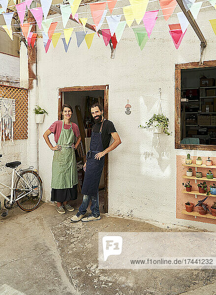 Smiling male and female design professionals standing with hand on hip at doorway