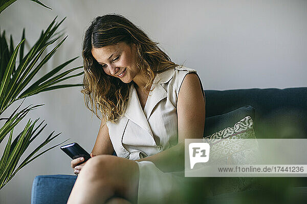 Smiling mid adult woman using smart phone in living room