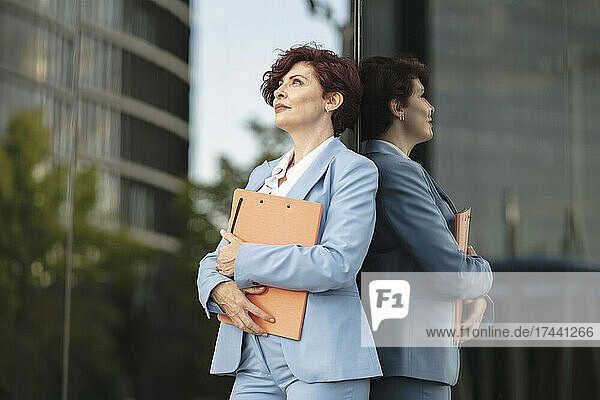 Businesswoman holding file while standing in front of glass wall
