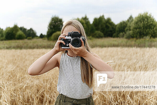 Blond girl photographing through camera on wheat field