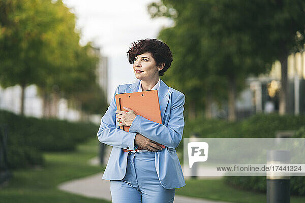 Eine berufstätige Frau hält eine Akte in der Hand  während sie im Büropark steht