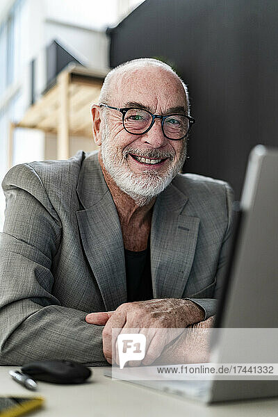 Smiling senior male professional sitting with laptop in studio