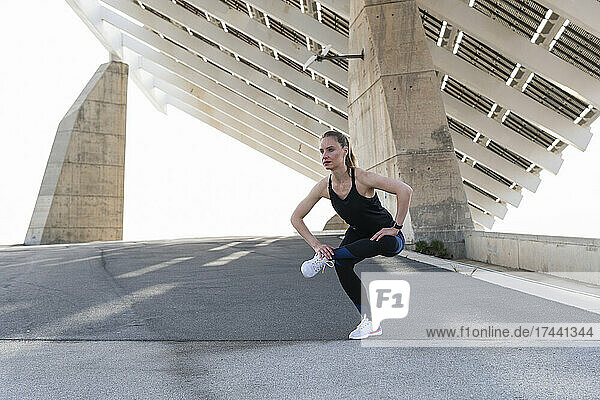 Female athlete warming up while stretching on road