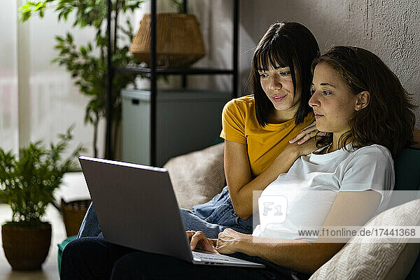 Lesbian couple using laptop while sitting on sofa at home