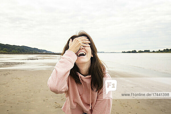Glückliche Frau  die am Strand die Augen mit der Hand bedeckt