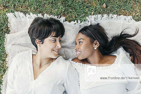 Smiling women looking at each other while lying on blanket