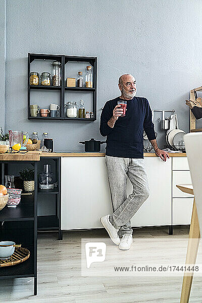 Senior man holding smoothie glass in kitchen at home