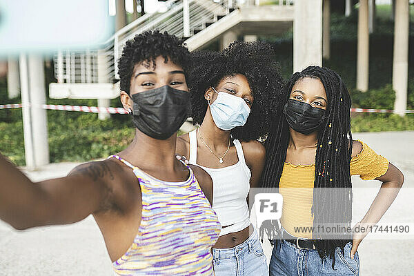Young women wearing protective face masks taking selfie during pandemic