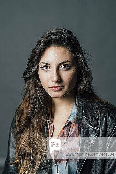 Young woman wearing leather jacket against gray background