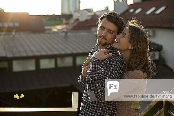 Girlfriend with brown hair hugging boyfriend on rooftop