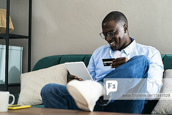 Smiling man paying through credit card while using digital tablet at home