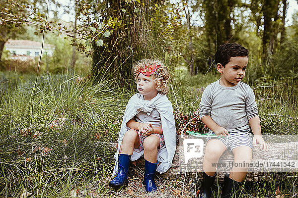 Cute boys wearing boots sitting on log in forest