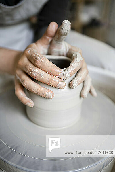 Young female potter making shape on pottery wheel in workshop