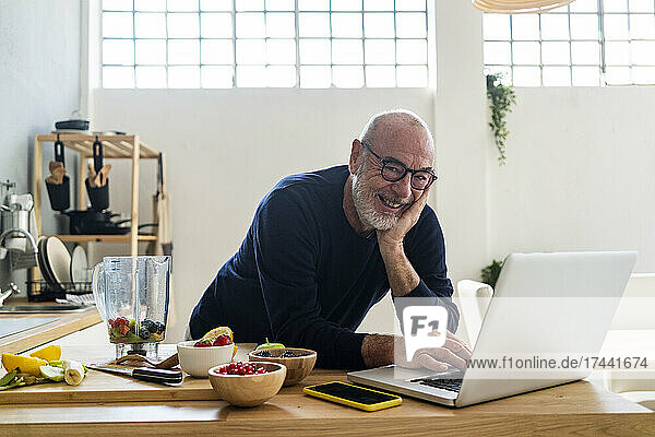 Smiling man with laptop leaning on kitchen counter
