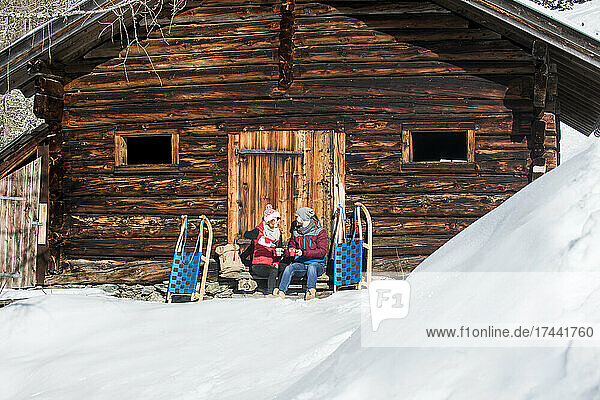 Paar genießt Getränk  während es im Winter in der Nähe der Hütte sitzt