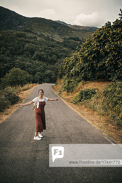 Happy woman with arms outstretched enjoying while standing on road