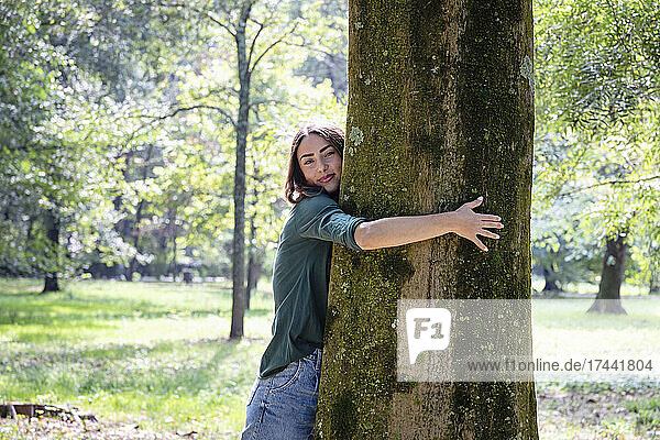 Beautiful young woman hugging tree in park